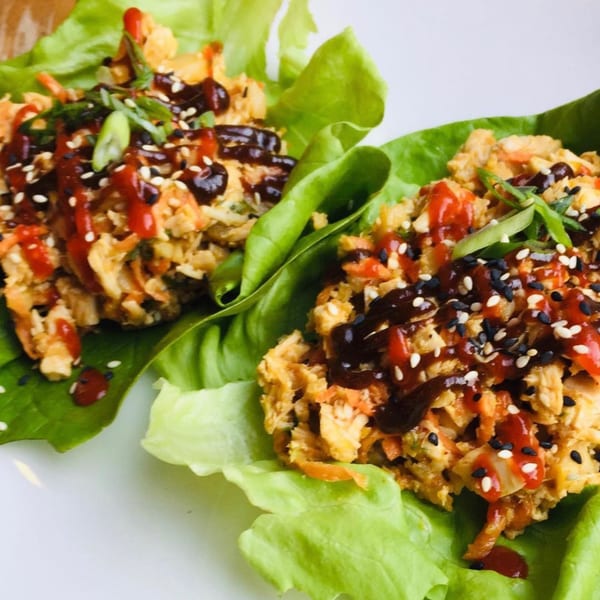 Two lettuce wraps filled with chicken, carrots, and sauce, garnished with sesame seeds and scallions.