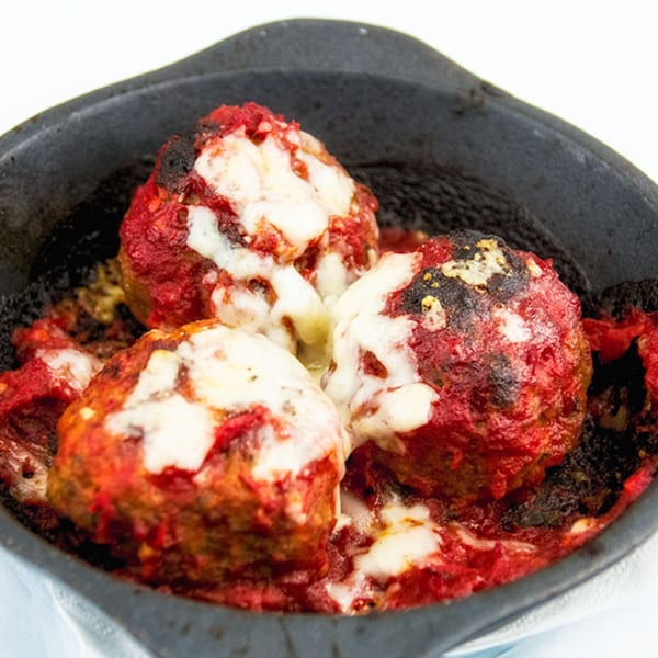 Three large meatballs covered in red sauce and melted white cheese in a black skillet.