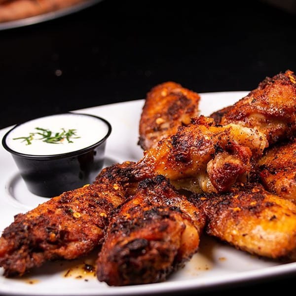 A plate of crispy, seasoned chicken wings with a side of ranch dressing garnished with dill.