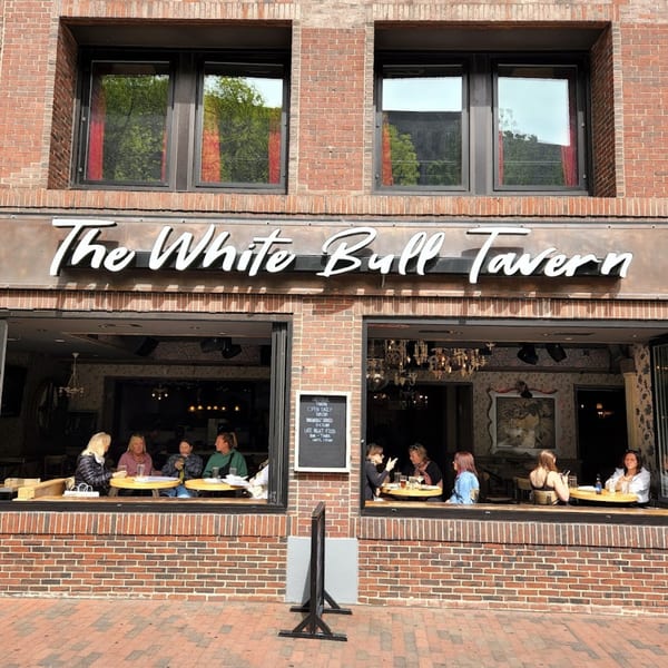 The White Bull Tavern's brick facade with large windows revealing patrons dining inside.