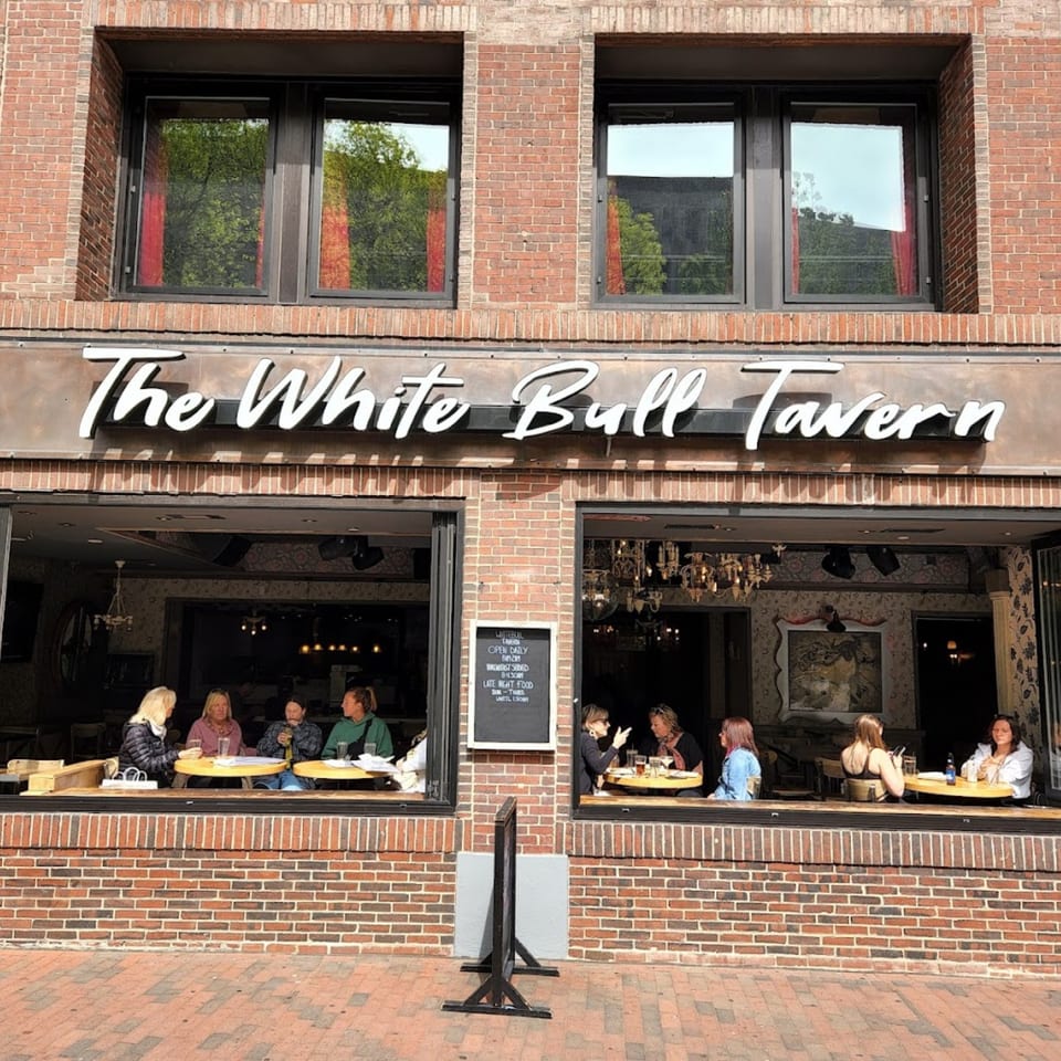 The White Bull Tavern's brick facade with large windows revealing patrons dining inside.