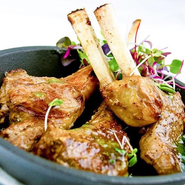 Grilled lamb chops with microgreens are served in a dark bowl at The White Bull Tavern.