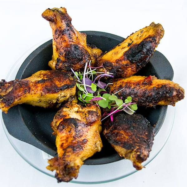 Six grilled chicken wings with charred skin and microgreens, served in a black cast iron dish.