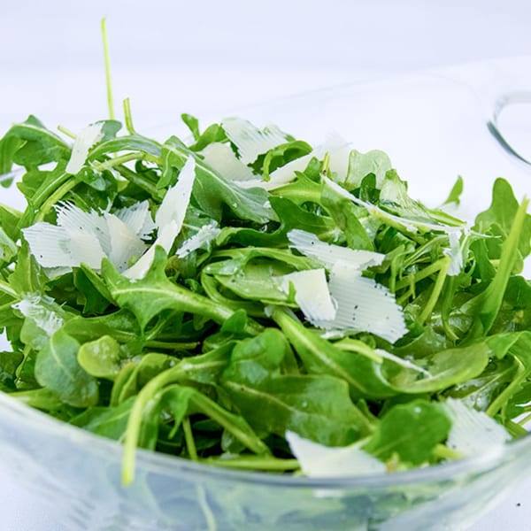 A glass bowl filled with fresh green arugula and shaved Parmesan cheese.